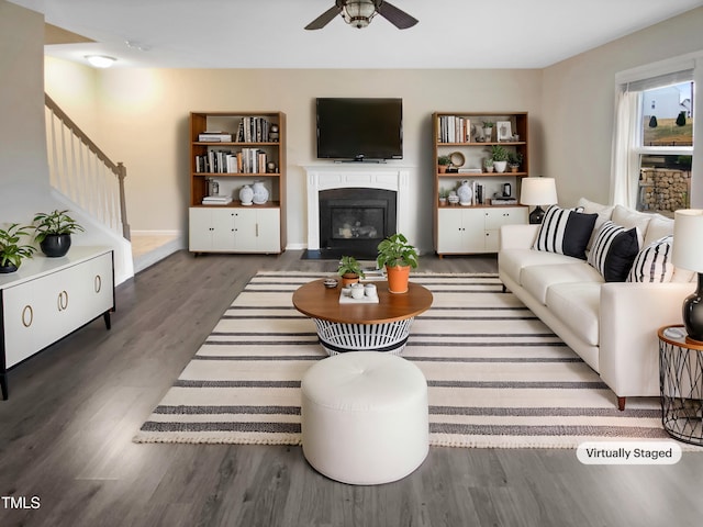 living room with a ceiling fan, stairway, a fireplace with flush hearth, and wood finished floors