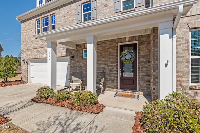 doorway to property featuring a garage, covered porch, and brick siding