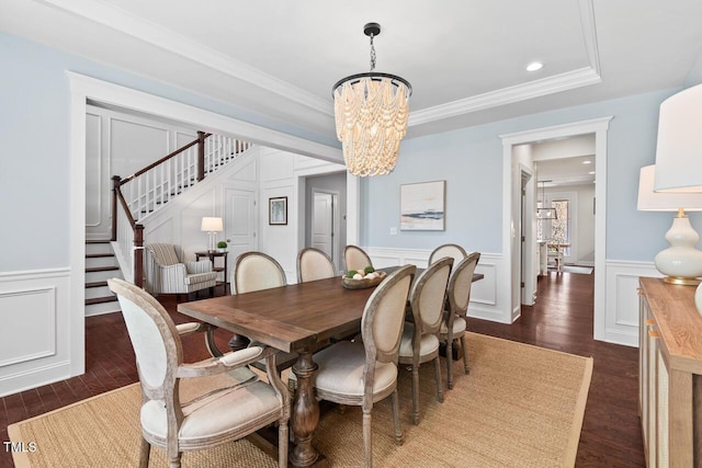 dining room featuring dark wood-type flooring, a chandelier, stairs, ornamental molding, and a decorative wall