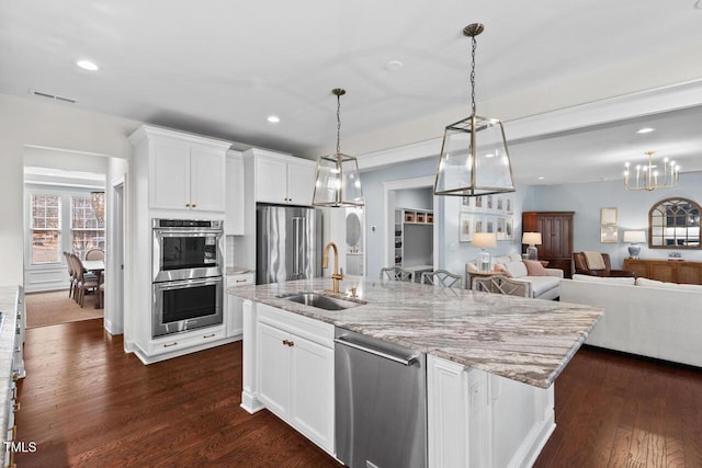 kitchen with an island with sink, dark wood-style flooring, a sink, stainless steel appliances, and white cabinetry