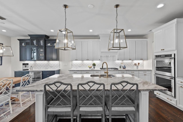 kitchen featuring glass insert cabinets, dark wood finished floors, double oven, a breakfast bar area, and hanging light fixtures