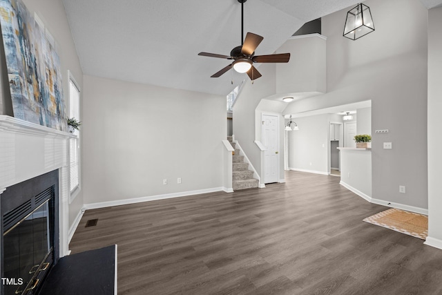 unfurnished living room with ceiling fan, baseboards, stairway, a glass covered fireplace, and dark wood-style flooring