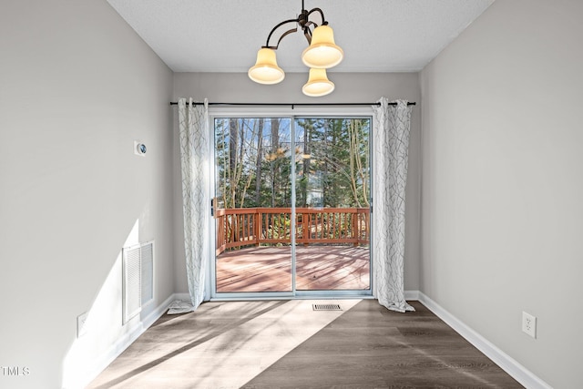 unfurnished dining area featuring visible vents, an inviting chandelier, baseboards, and wood finished floors