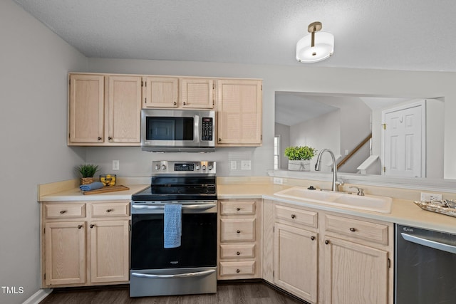 kitchen with light brown cabinetry, stainless steel appliances, light countertops, and a sink