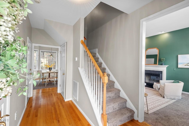 staircase featuring a glass covered fireplace, baseboards, visible vents, and wood finished floors