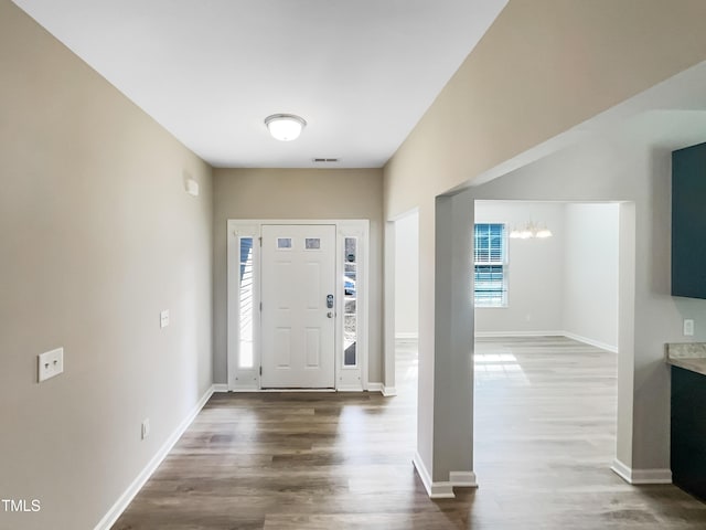 foyer entrance with visible vents, baseboards, a notable chandelier, and wood finished floors