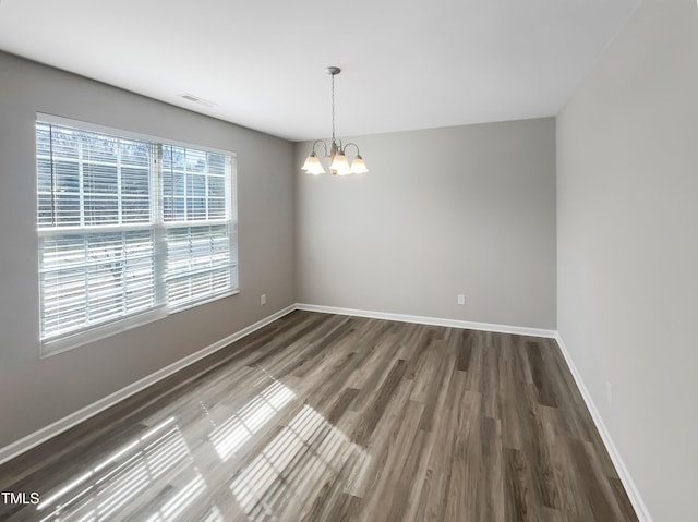 empty room with visible vents, an inviting chandelier, baseboards, and wood finished floors