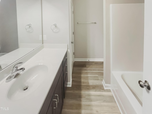 bathroom featuring baseboards, a tub to relax in, wood finished floors, and vanity