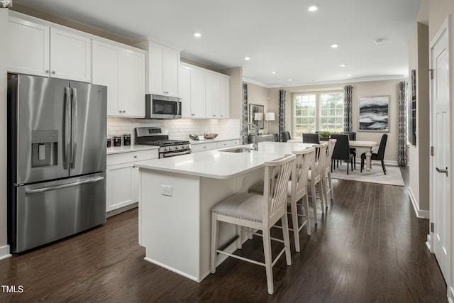 kitchen with a sink, backsplash, dark wood-style flooring, appliances with stainless steel finishes, and a kitchen island with sink