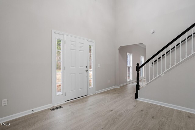 foyer featuring visible vents, baseboards, stairway, a towering ceiling, and wood finished floors