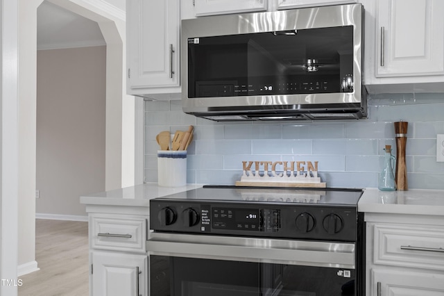 kitchen with ornamental molding, stainless steel microwave, range with electric stovetop, white cabinets, and light countertops