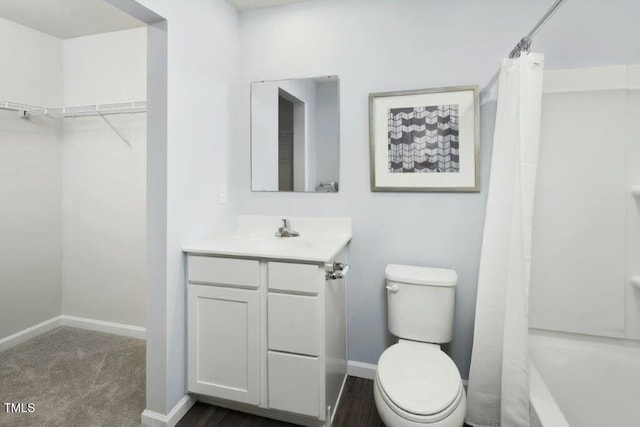 bathroom with a spacious closet, toilet, vanity, and baseboards