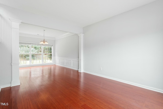 spare room with a chandelier, decorative columns, wainscoting, a decorative wall, and dark wood-style flooring