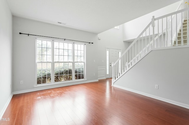 unfurnished living room with visible vents, baseboards, wood finished floors, and stairs