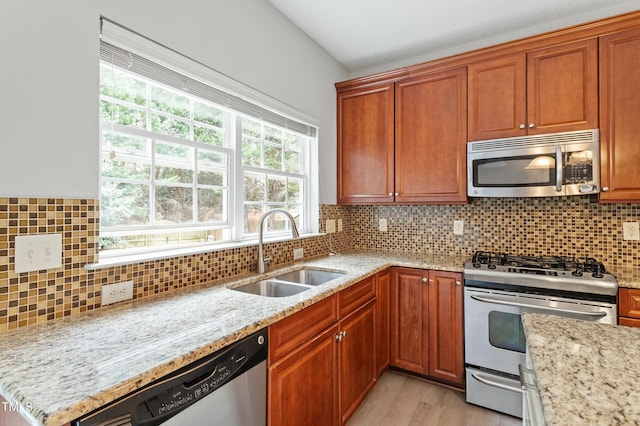 kitchen with decorative backsplash, light stone countertops, stainless steel appliances, and a sink