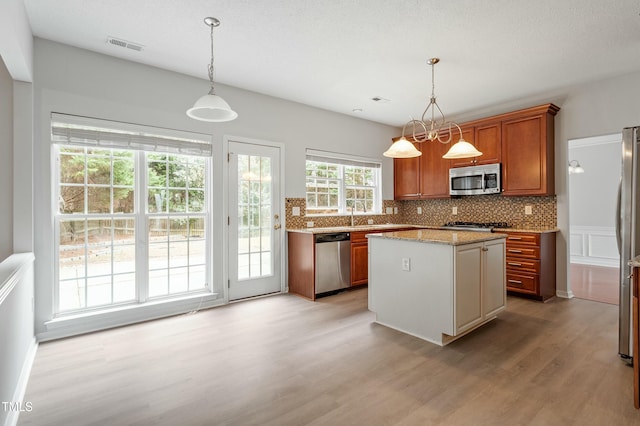 kitchen featuring visible vents, a kitchen island, decorative backsplash, light wood-style flooring, and appliances with stainless steel finishes