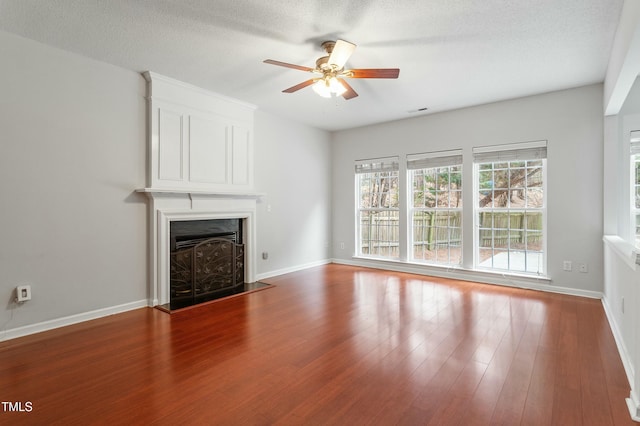 unfurnished living room featuring a ceiling fan, wood finished floors, baseboards, a fireplace with flush hearth, and a textured ceiling