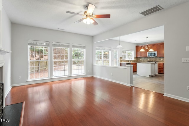 unfurnished living room with a ceiling fan, visible vents, baseboards, a fireplace, and light wood-style floors