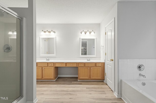 bathroom with a sink, a textured ceiling, wood finished floors, double vanity, and a bath