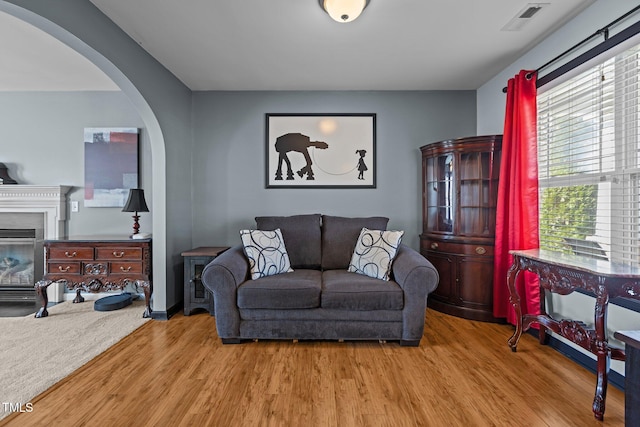 living area featuring a glass covered fireplace, visible vents, arched walkways, and wood finished floors