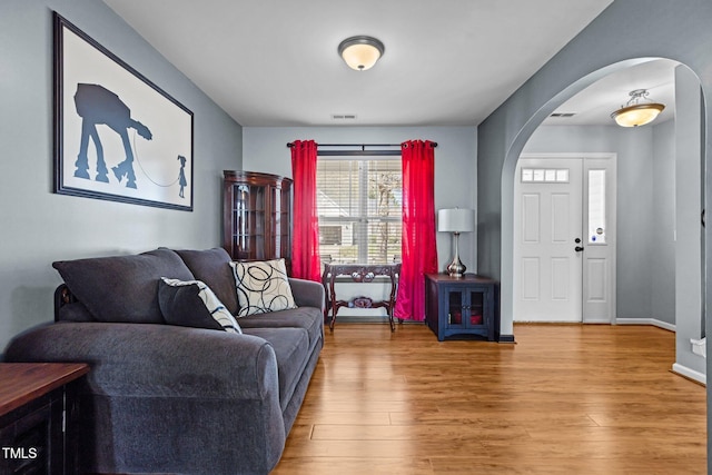 living area featuring baseboards, wood finished floors, visible vents, and arched walkways