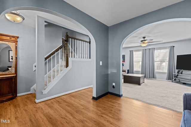 interior space with ceiling fan, baseboards, stairs, wood finished floors, and arched walkways