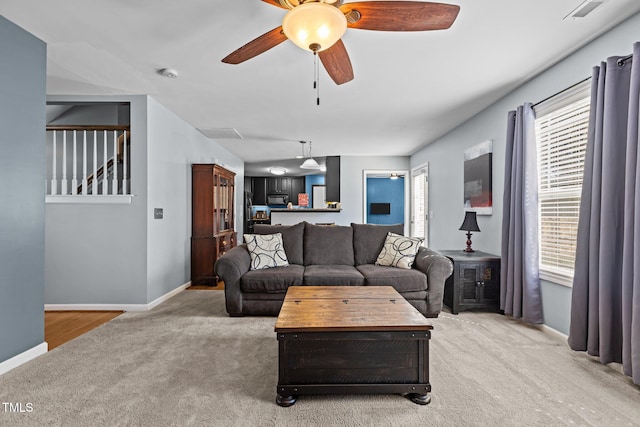 living room featuring stairway, light colored carpet, baseboards, and ceiling fan