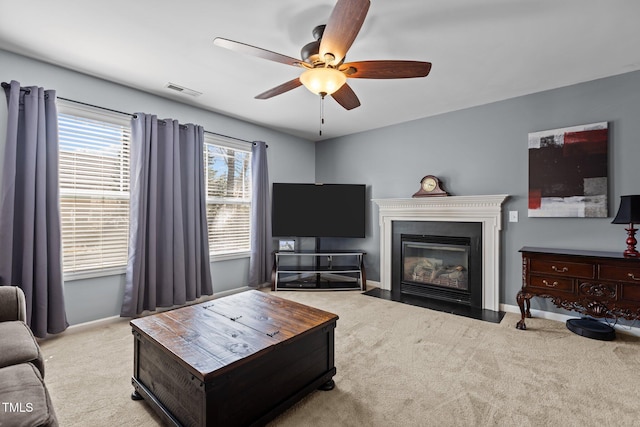 living room with a ceiling fan, visible vents, baseboards, a fireplace with flush hearth, and carpet flooring