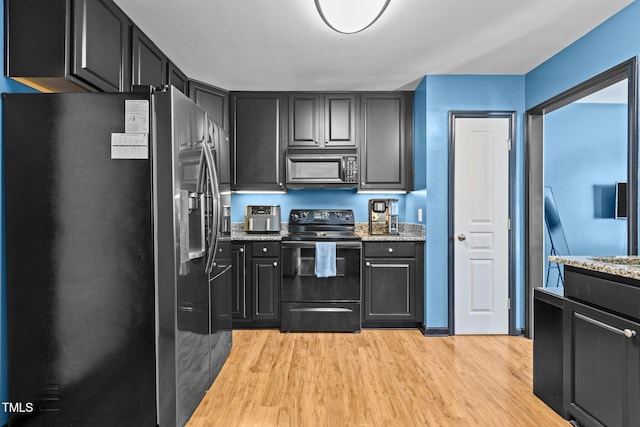 kitchen featuring dark cabinets, light wood-style flooring, black appliances, and light stone countertops