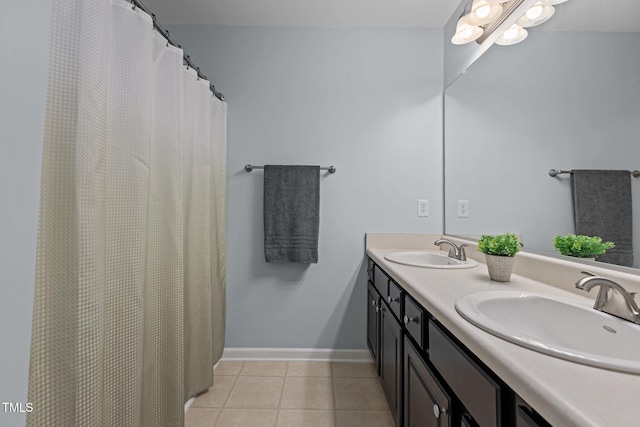 full bath with tile patterned floors, double vanity, baseboards, and a sink