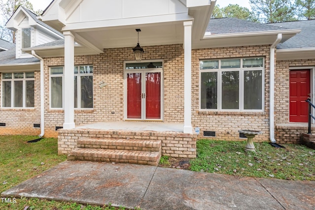 property entrance with a shingled roof, a porch, brick siding, and crawl space