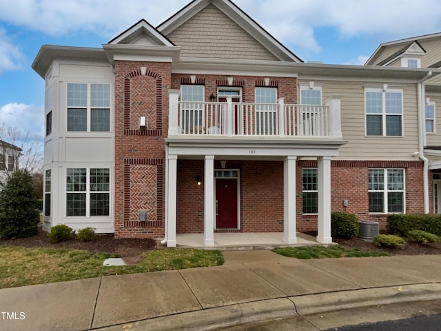 view of front of property featuring central AC unit, brick siding, covered porch, and a balcony