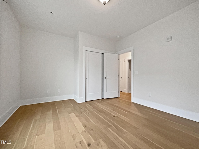 unfurnished bedroom featuring wood finished floors, baseboards, and a closet