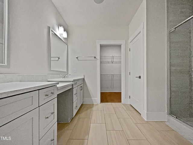 bathroom featuring wood finish floors, a walk in closet, a stall shower, baseboards, and vanity