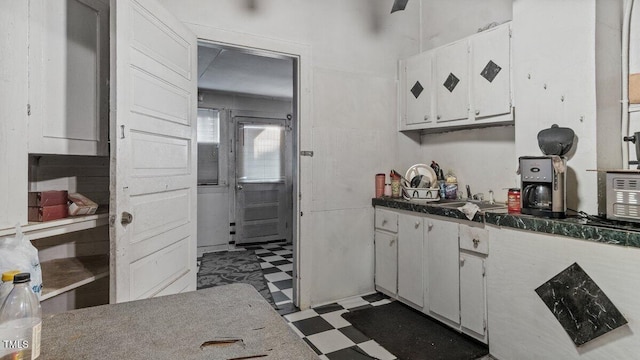 kitchen with white cabinetry, tile patterned floors, dark countertops, and a sink