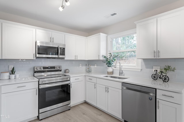 kitchen featuring light countertops, decorative backsplash, appliances with stainless steel finishes, white cabinetry, and a sink