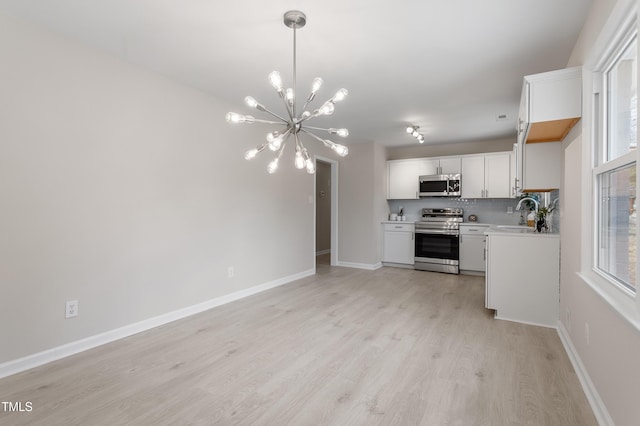 kitchen with stainless steel appliances, hanging light fixtures, light countertops, light wood-type flooring, and a chandelier