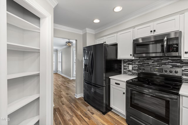 kitchen featuring crown molding, black appliances, light countertops, and wood finished floors