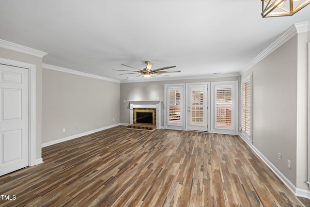 unfurnished living room featuring wood finished floors, crown molding, baseboards, a brick fireplace, and ceiling fan