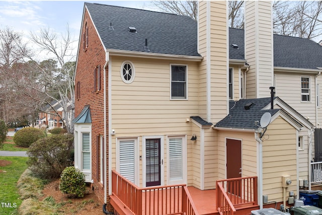 back of property featuring brick siding, roof with shingles, and a chimney