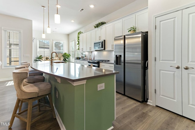 kitchen with tasteful backsplash, an island with sink, appliances with stainless steel finishes, wood finished floors, and a sink