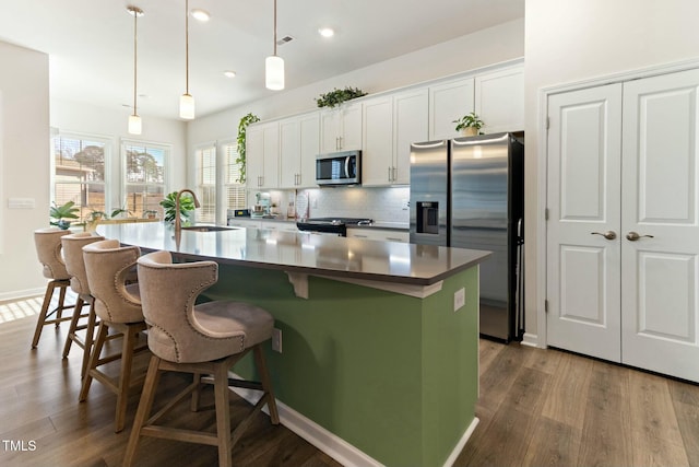 kitchen featuring backsplash, a large island with sink, appliances with stainless steel finishes, dark wood-style floors, and a sink