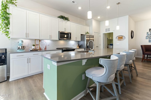 kitchen featuring visible vents, a kitchen island with sink, a sink, decorative backsplash, and appliances with stainless steel finishes