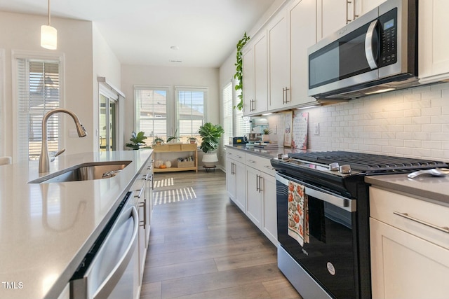 kitchen with backsplash, decorative light fixtures, wood finished floors, stainless steel appliances, and a sink