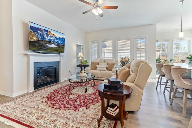 living room with a glass covered fireplace, baseboards, wood finished floors, and a ceiling fan