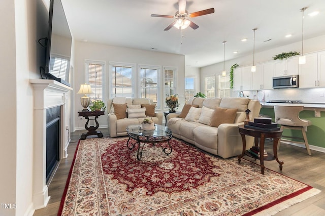 living area with wood finished floors, a ceiling fan, baseboards, recessed lighting, and a high end fireplace