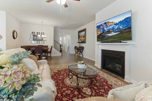 living room featuring a glass covered fireplace, ceiling fan with notable chandelier, baseboards, and wood finished floors