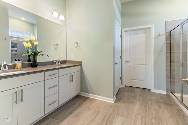 full bath featuring double vanity, a shower stall, baseboards, and a sink