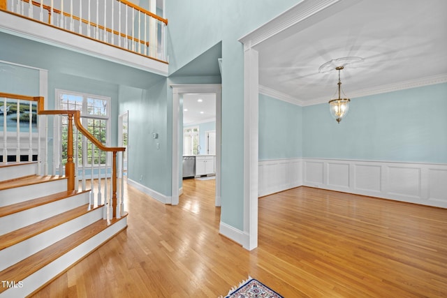 foyer featuring ornamental molding, wood finished floors, wainscoting, baseboards, and stairs