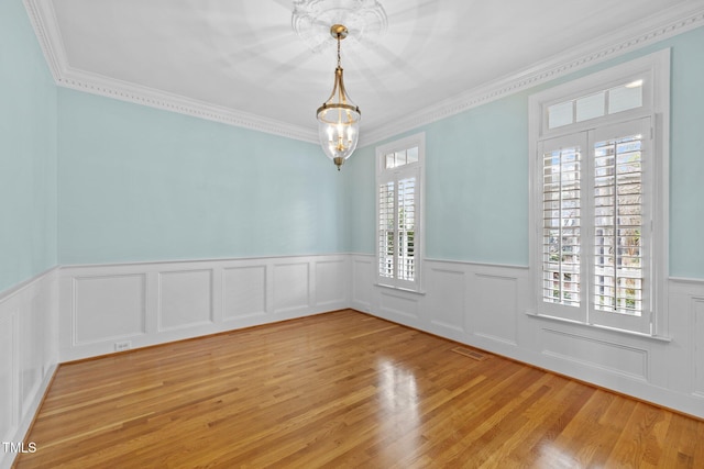 spare room with visible vents, a notable chandelier, ornamental molding, wainscoting, and light wood finished floors